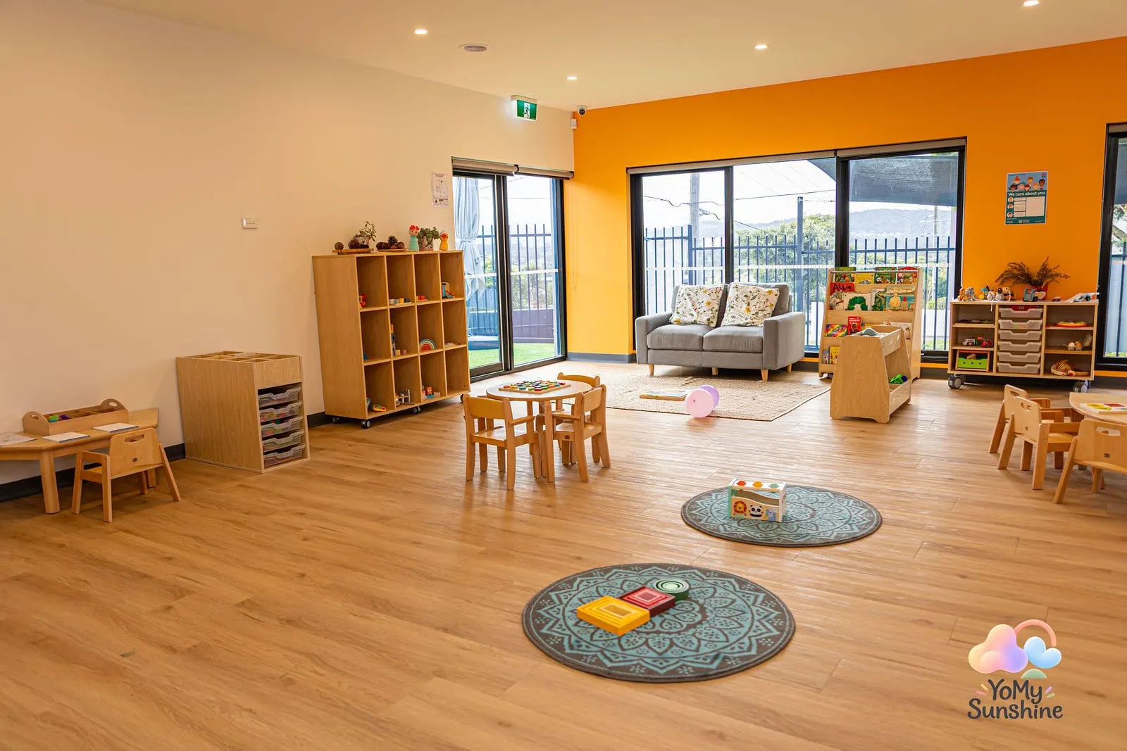 Learning room with an orange feature wall, round rugs, small timber tables and a couch corner