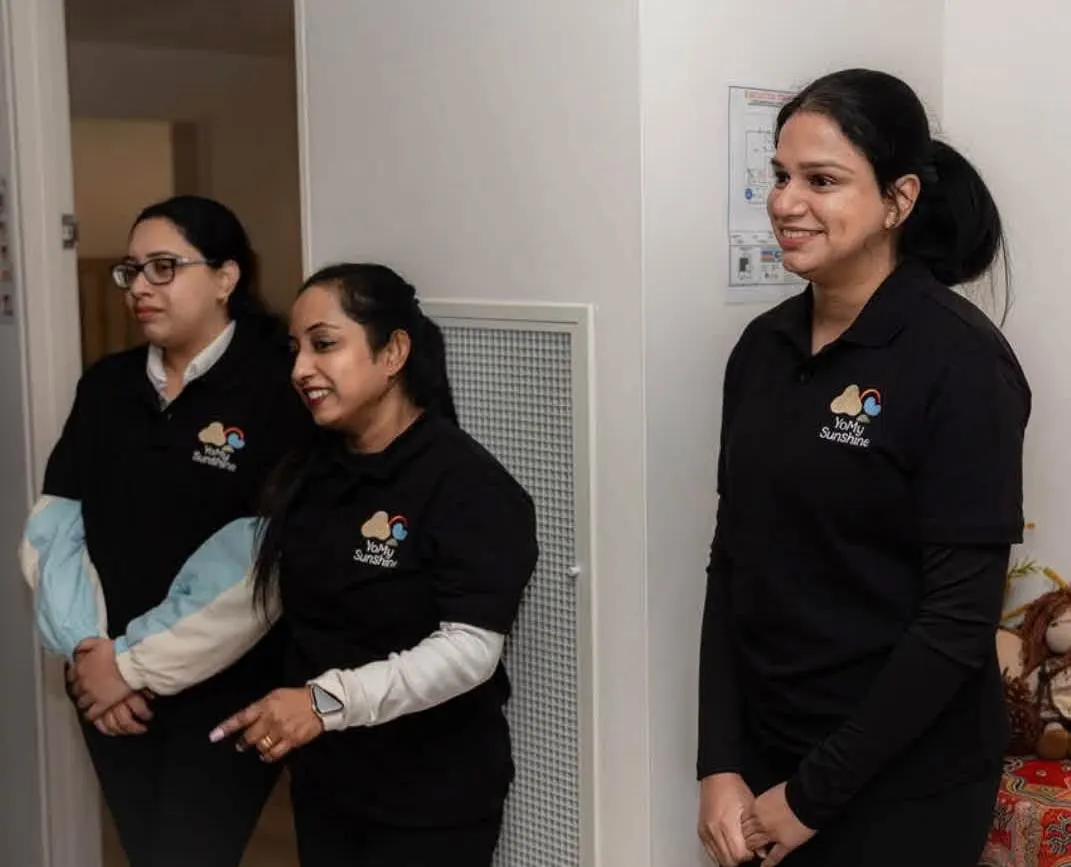 Three YoMySunshine educators in black centre polo shirts standing together inside the centre